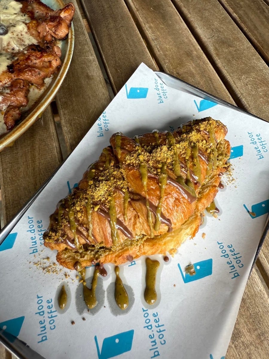 A croissant drizzled with pistachio and chocolate on a Blue Door Coffee branded paper tray